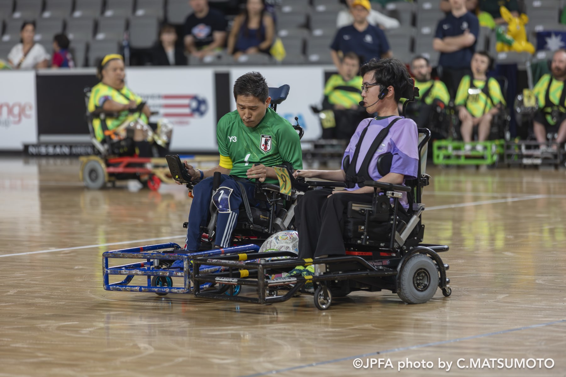 足元のガード（バンパー）でボールを競り合うパワーチェアフットボールの選手2人